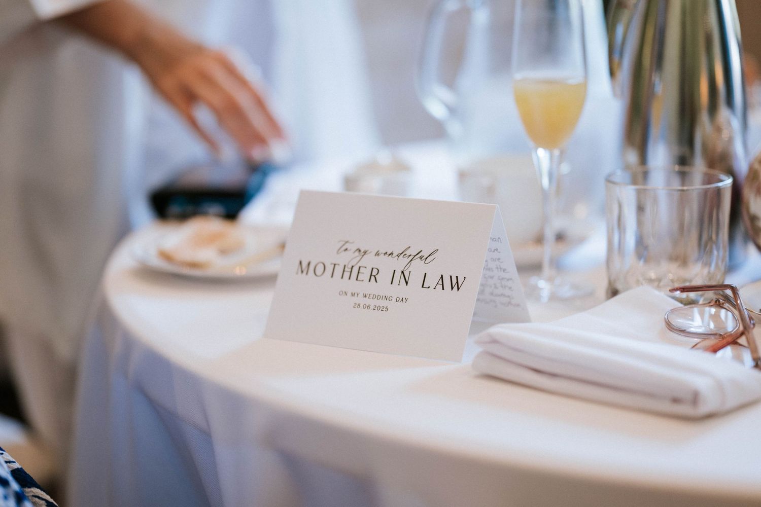Wedding place card for Mother-in-Law with champagne glass on elegant white tablecloth.