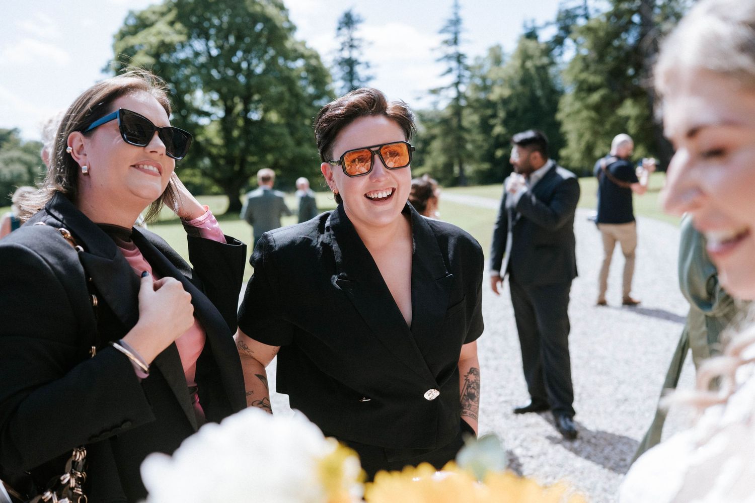 Candid wedding guest interactions captured in bright outdoor setting.