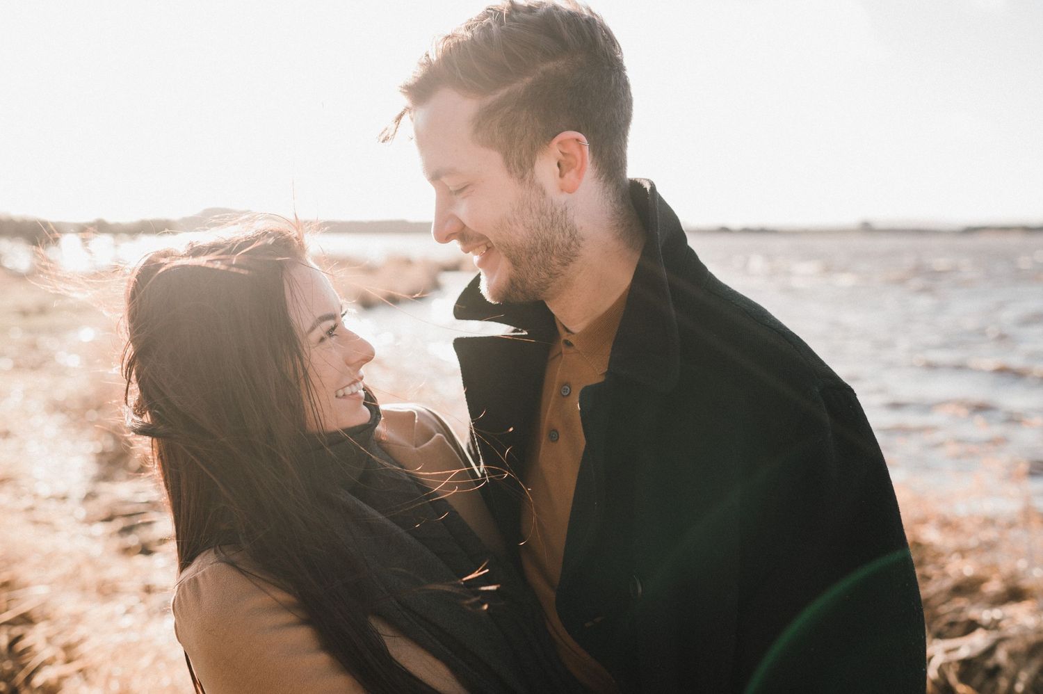 A couple shares an intimate moment on a rocky beach at sunset with golden light illuminating their silhouettes.