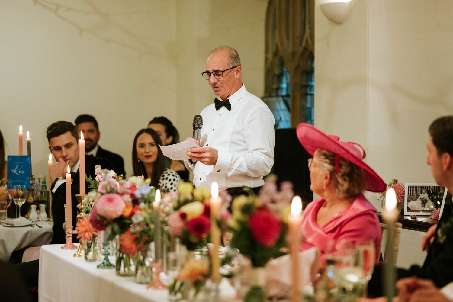 Wedding reception guests enjoying dinner and conversation at elegant tables with floral centerpieces.