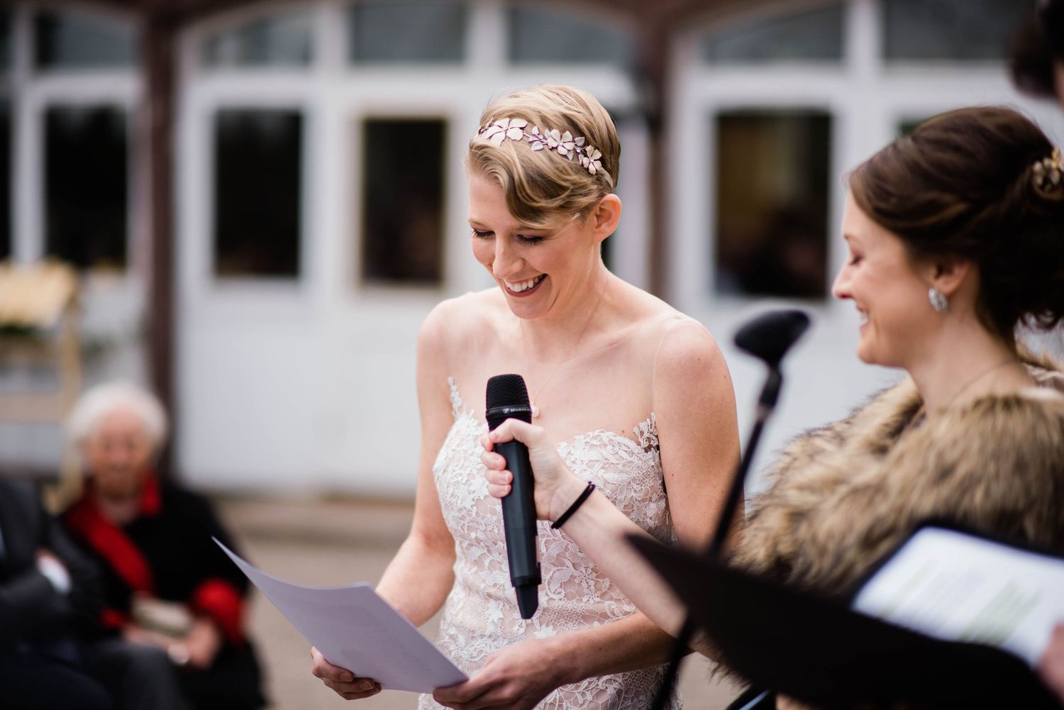 A person in a bridal gown speaks into a microphone during an outdoor ceremony.