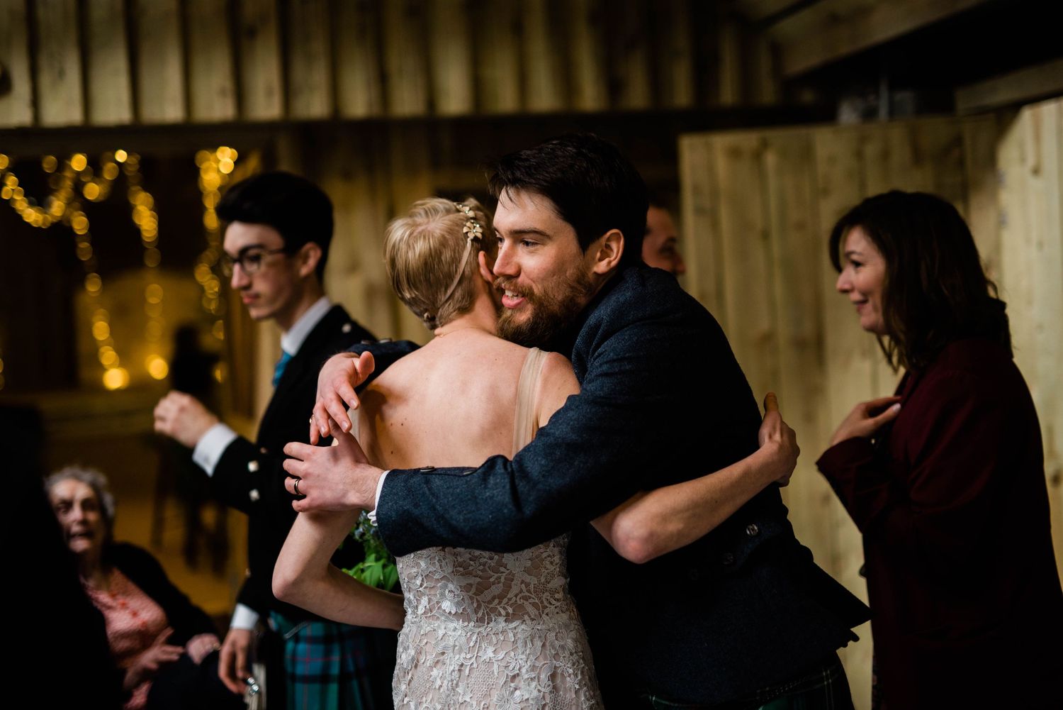 Tender moment during wedding reception with traditional Scottish attire and warm lighting.