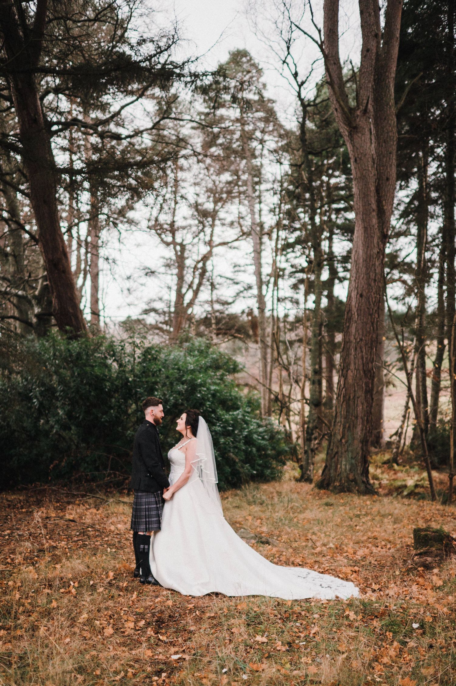 Wedding couple poses in a scenic forest setting with tall pine trees in the background.