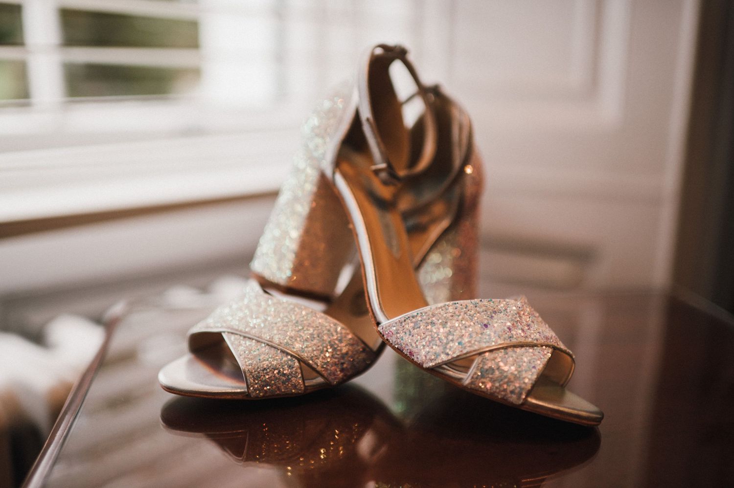 Glittery gold wedding heels with crossed straps displayed on dark surface.