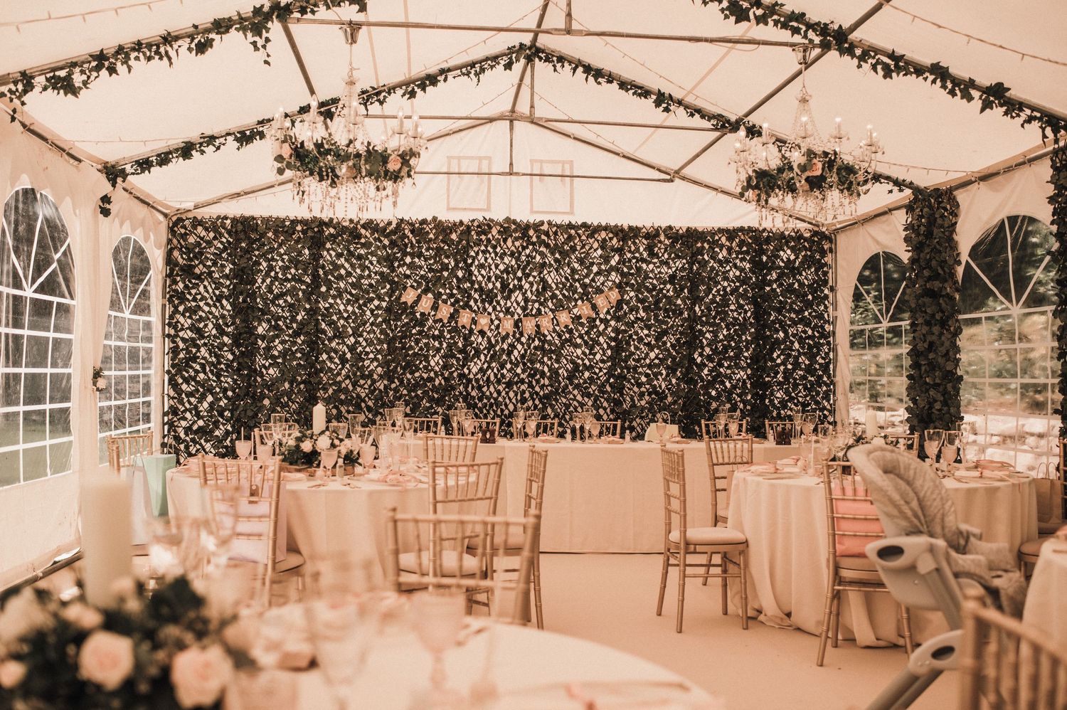 Wedding reception tent with twinkling lights and floral wall backdrop.