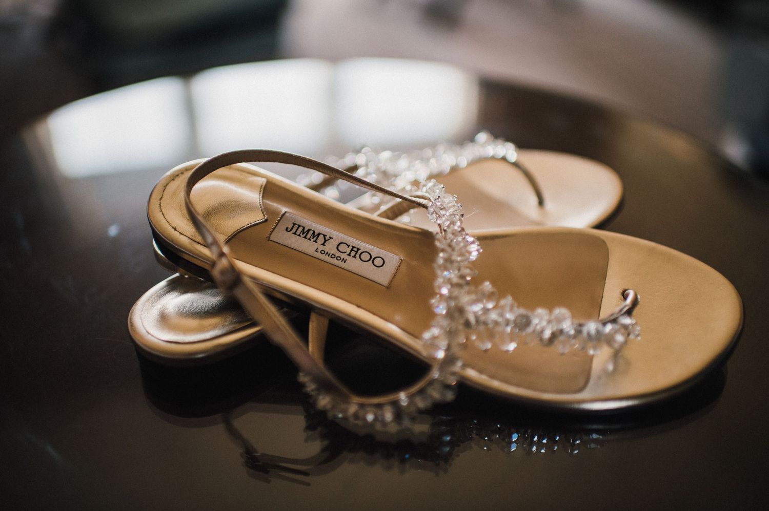Jimmy Choo sandals with crystal embellishments on dark surface.