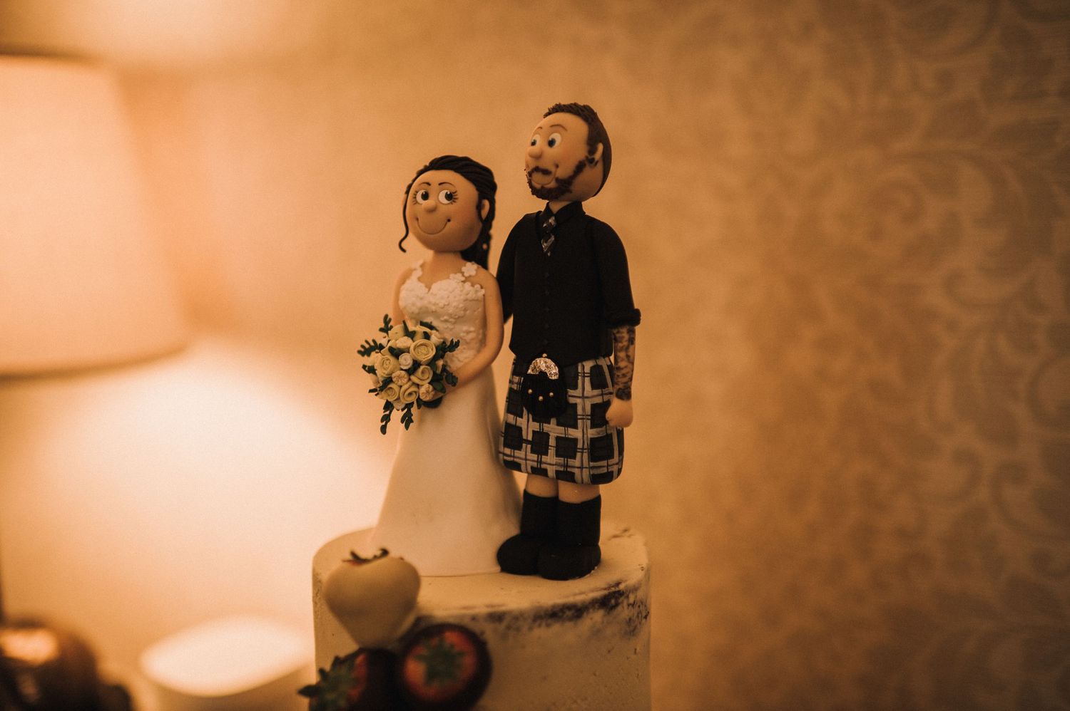 Wedding cake topper figurines with traditional Scottish attire displayed in warm lighting.