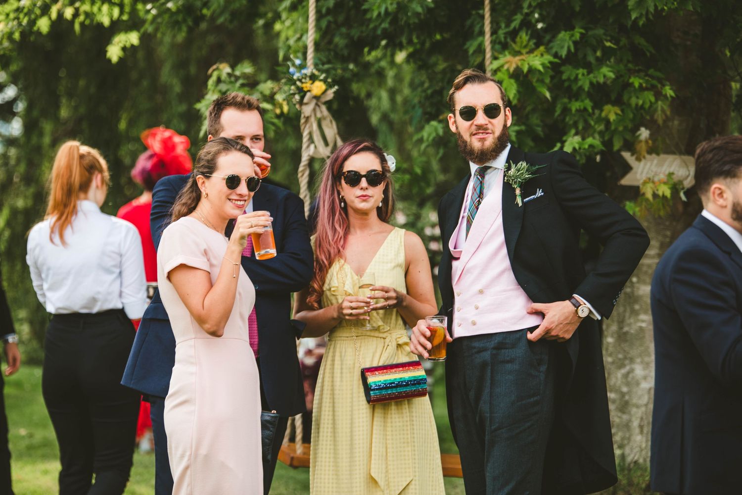 Stylish wedding guests in sunglasses enjoying drinks at outdoor reception.