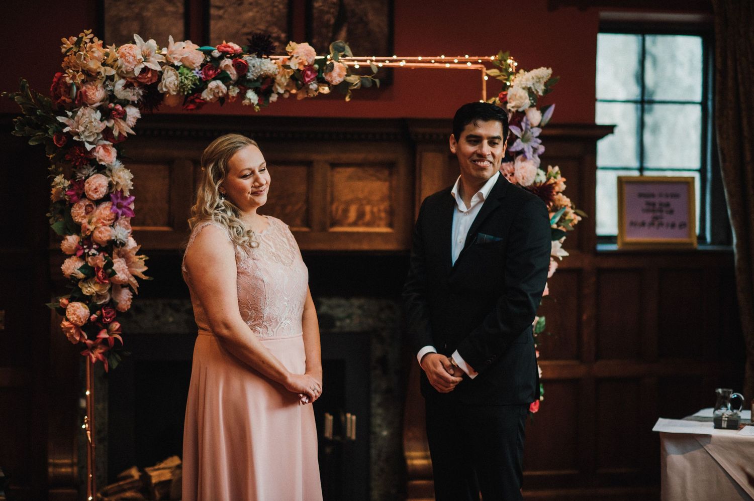 A couple stands beneath a decorative floral arch during their indoor ceremony.