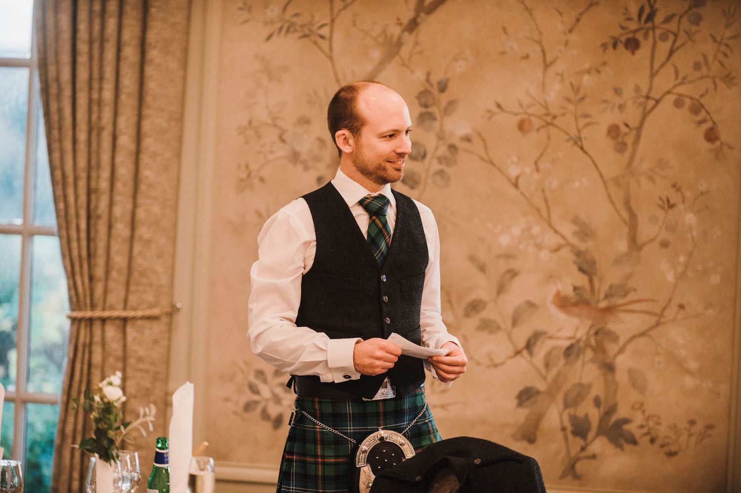 A man in traditional Scottish attire delivers a speech at a formal event.