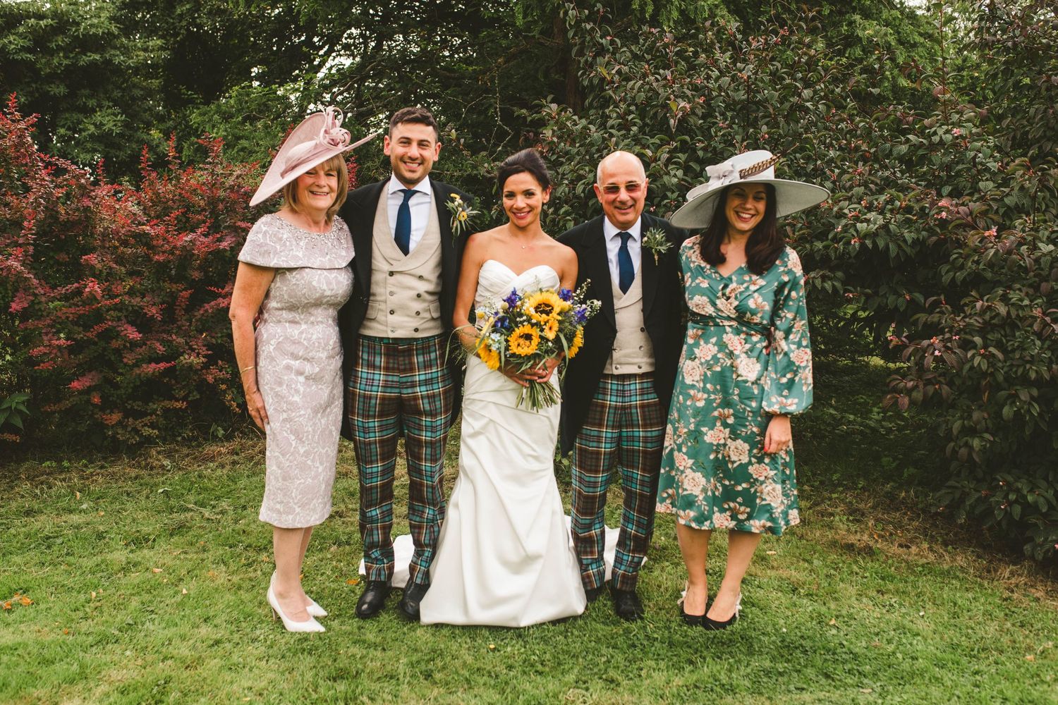 Family photo at Scottish wedding with traditional kilts and formal attire on green lawn.