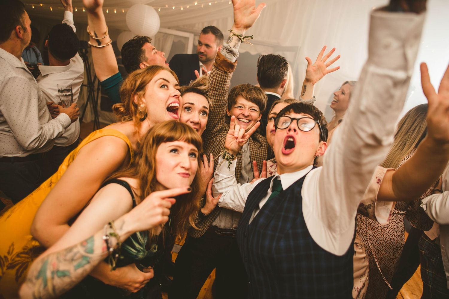Wedding party guests dancing and singing enthusiastically at a lively reception celebration.