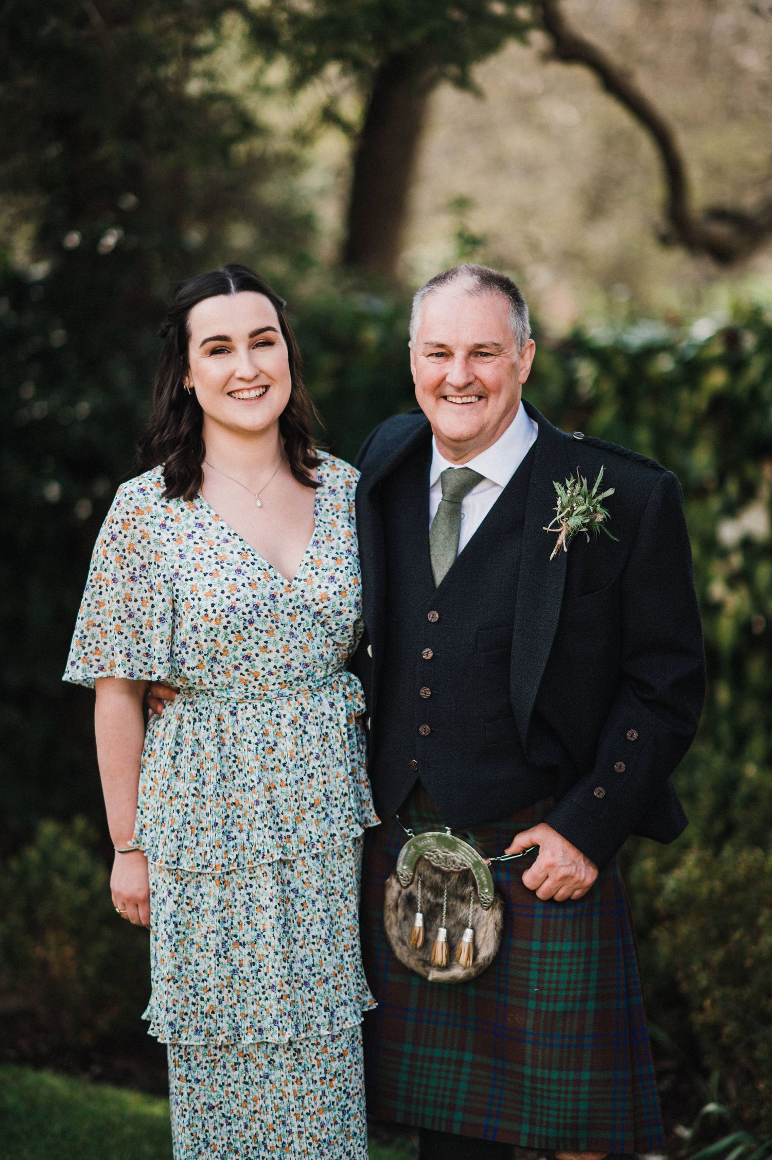 Wedding guests in Scottish attire standing together in garden setting.
