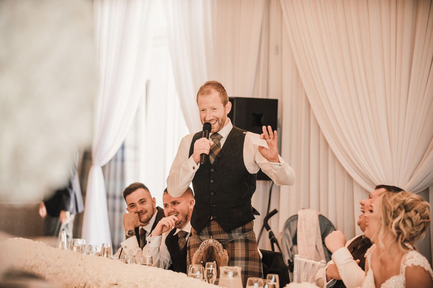 Speaker delivers emotional wedding toast while standing at decorated head table.