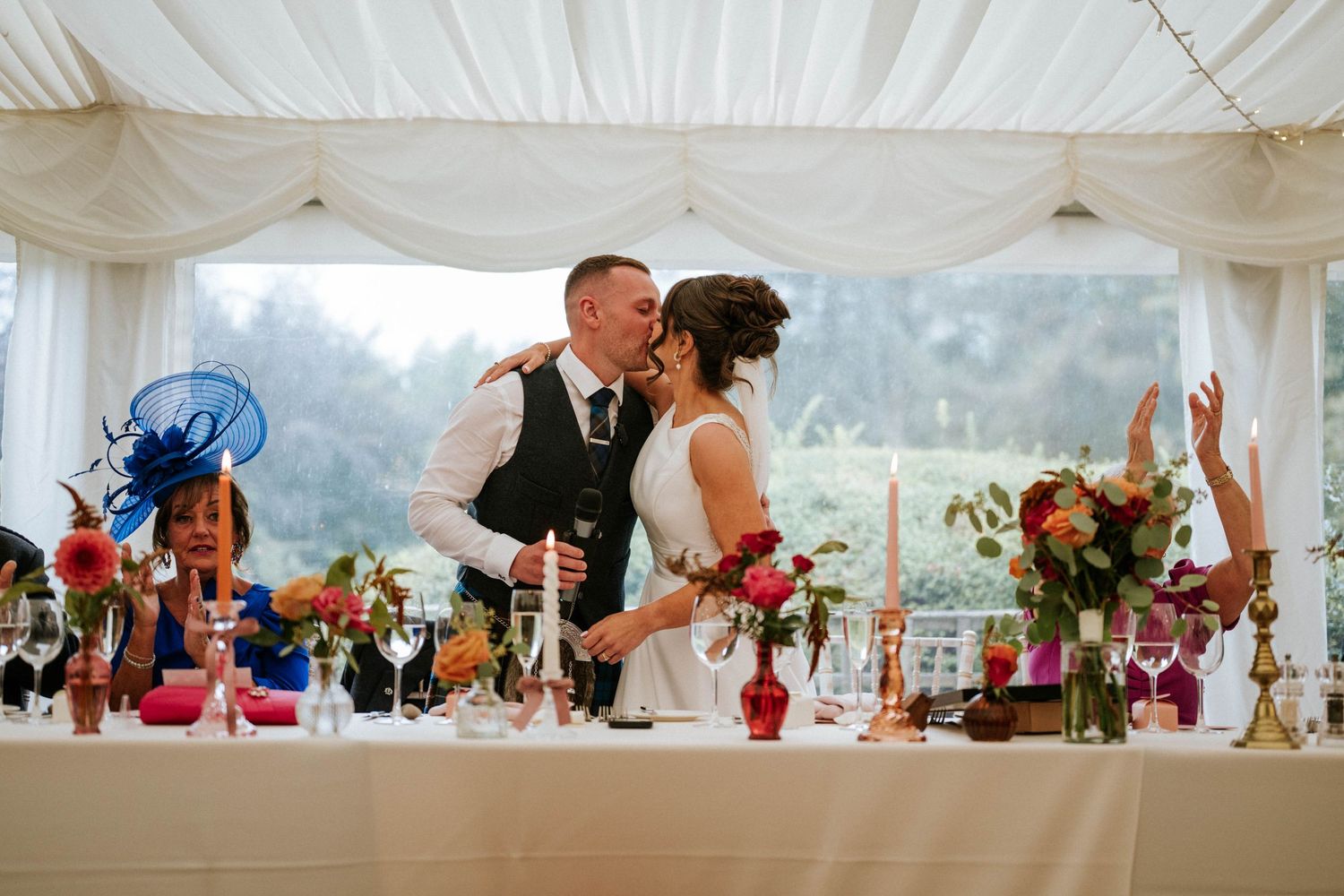 Panoramic view of a wedding celebration inside an elegant white tent with floral decorations.