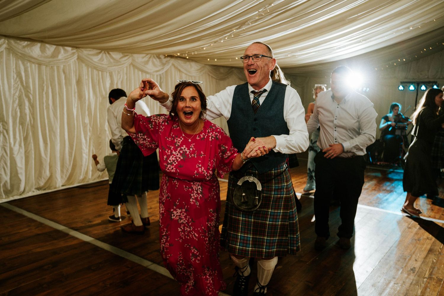 Wedding reception dance party with guests celebrating under elegant white draped ceiling.