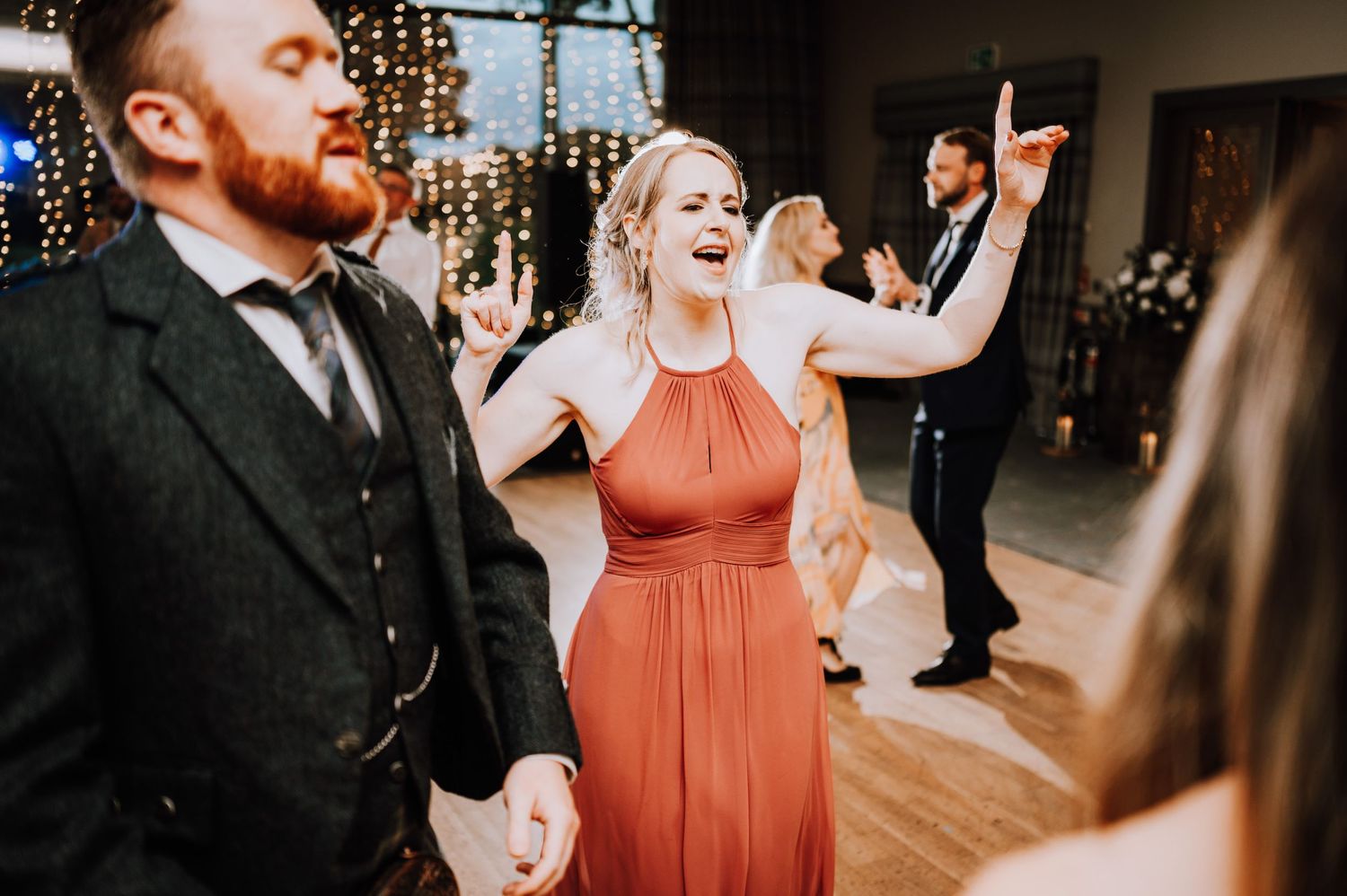 Wedding guests dance and celebrate on the dance floor under decorative string lights.