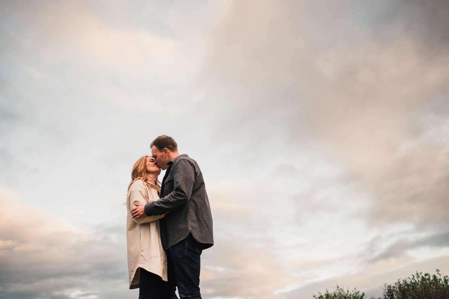 A tender moment captured between a couple against a dramatic sunset sky.