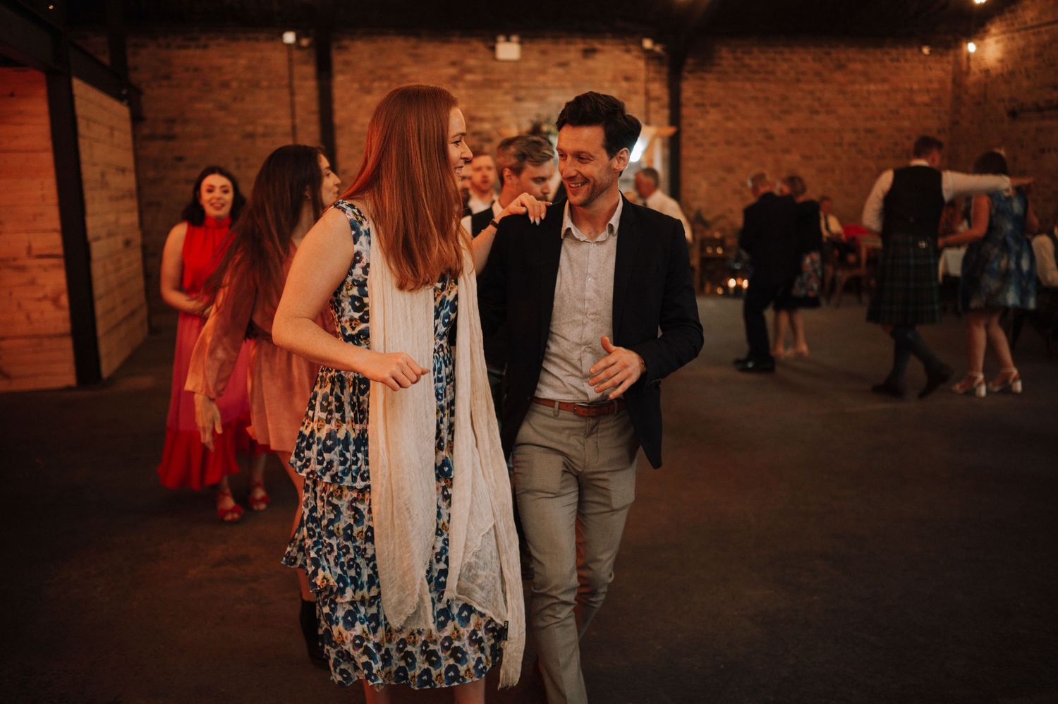 Guests mingle and socialize at an indoor wedding reception with warm lighting and brick walls.
