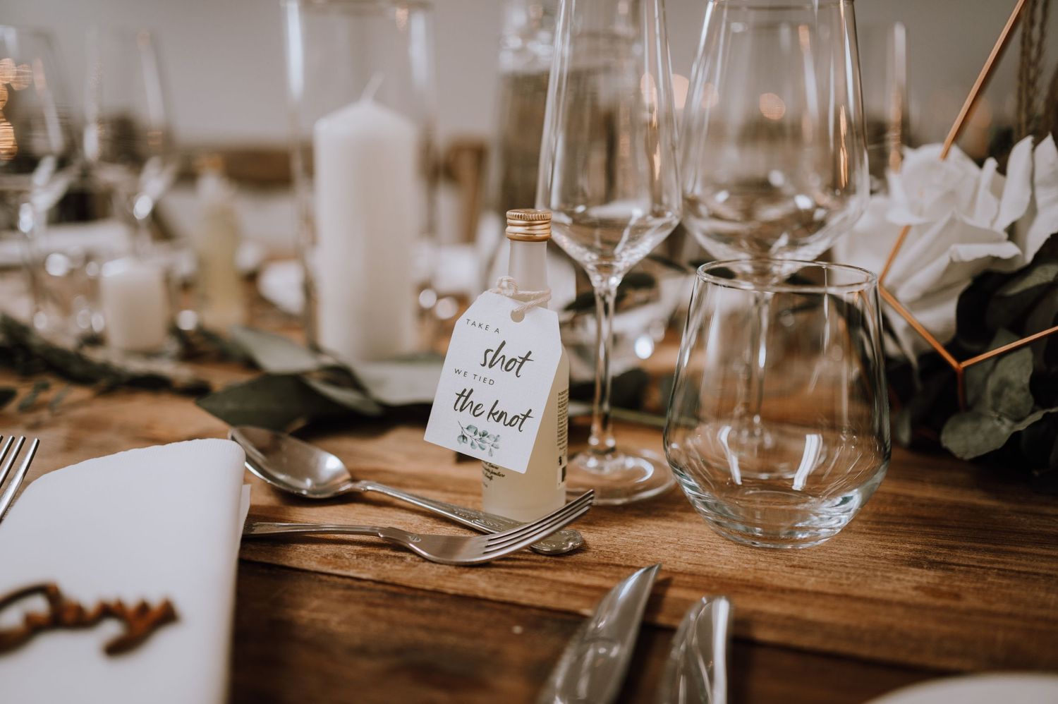 Rustic wedding table decor with wooden elements, glass name tags, and white candles.