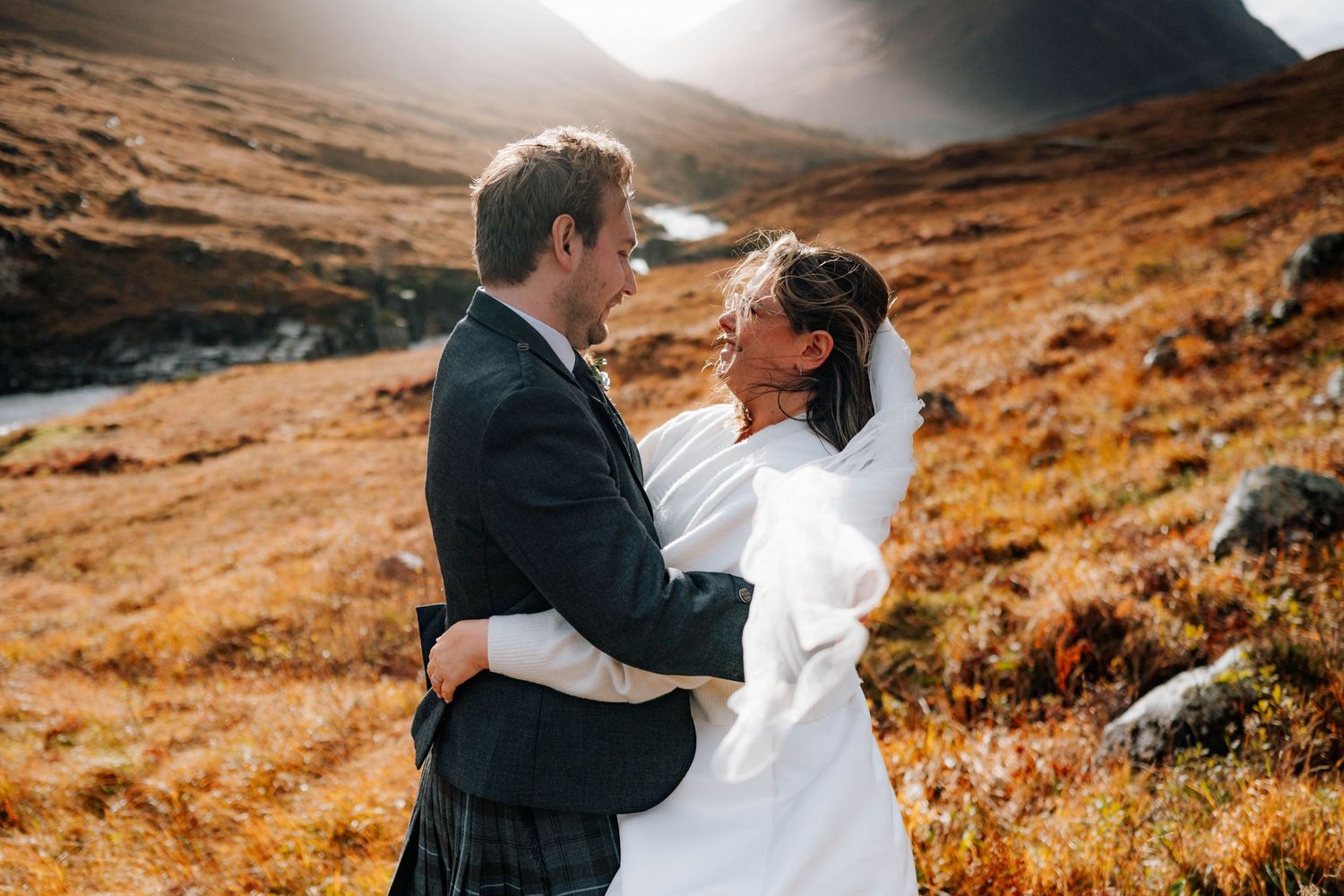 Couple embraces against dramatic mountainous landscape during golden hour.