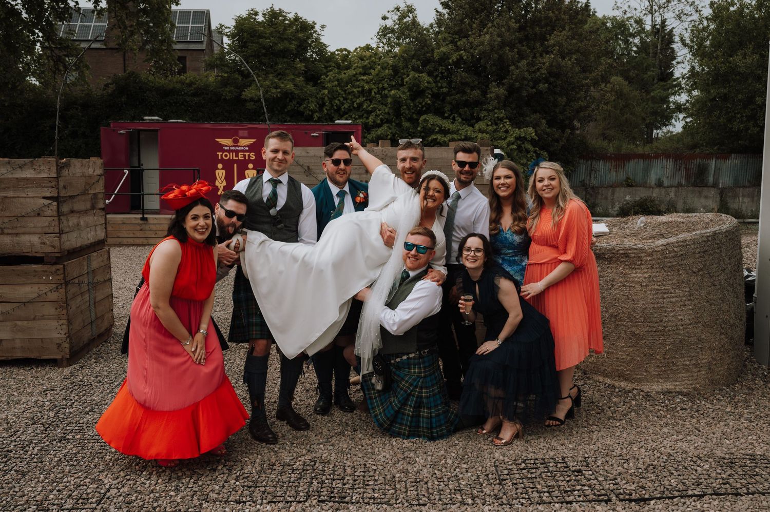Wedding party poses together for group photo with colorful attire and traditional Scottish elements.