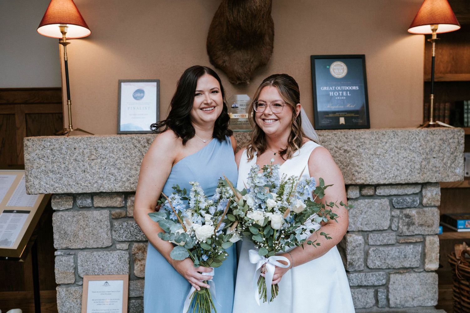 Wedding party members in light blue dresses pose together holding white floral bouquets.