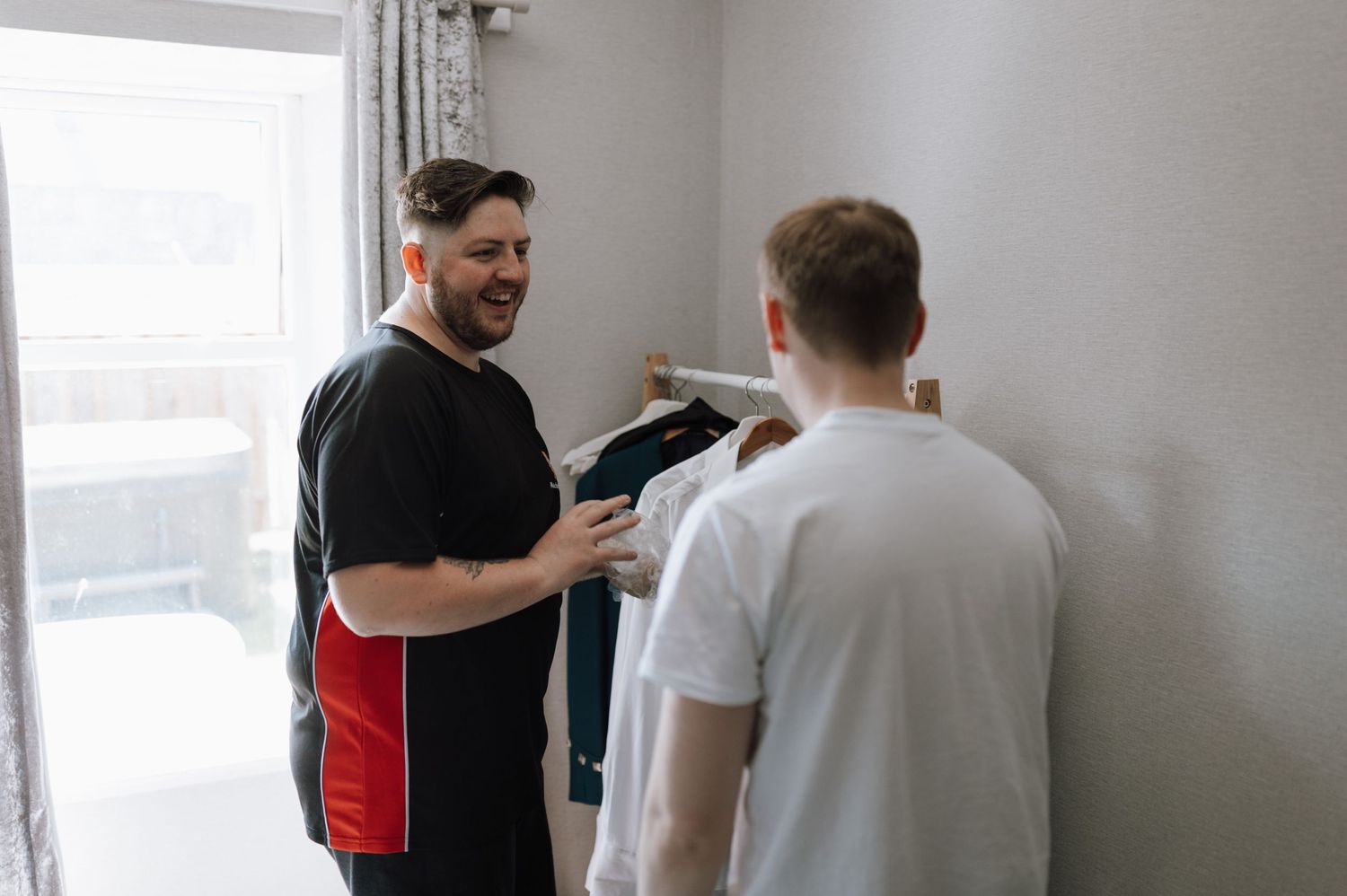 Two people helping with formal attire preparations indoors.