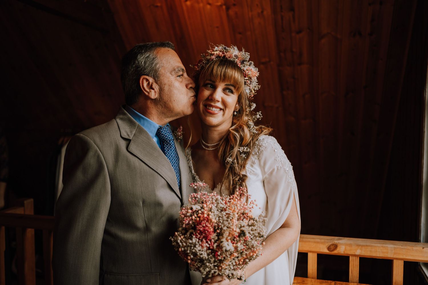 An intimate wedding moment between a couple in a wooden interior with warm lighting and floral details.