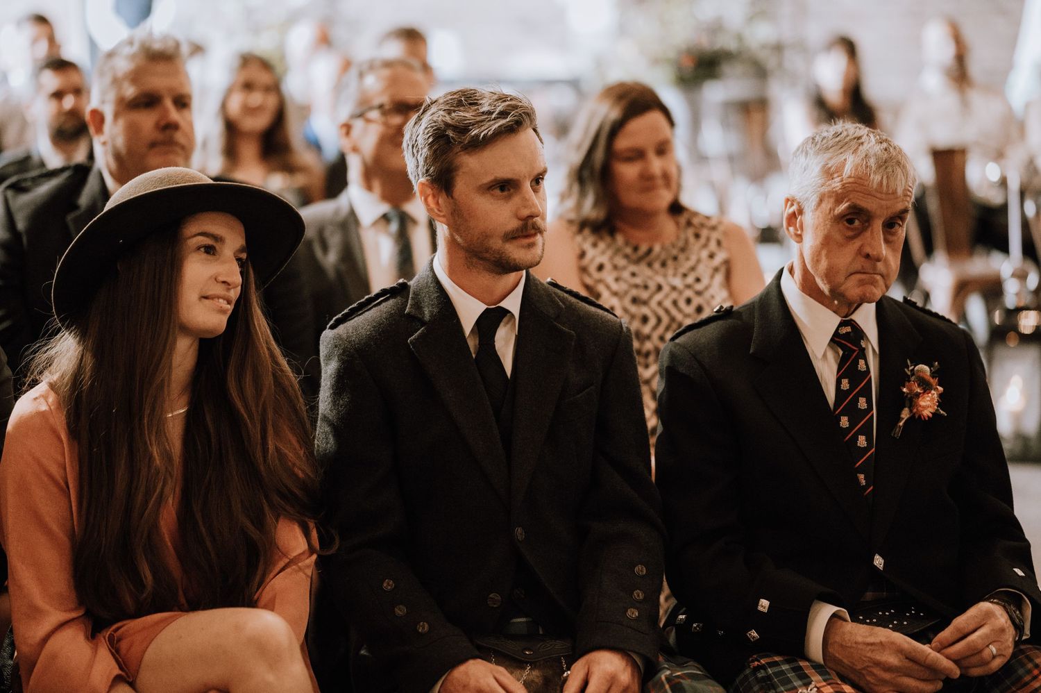 Wedding guests seated in rows during indoor ceremony with exposed brick walls.