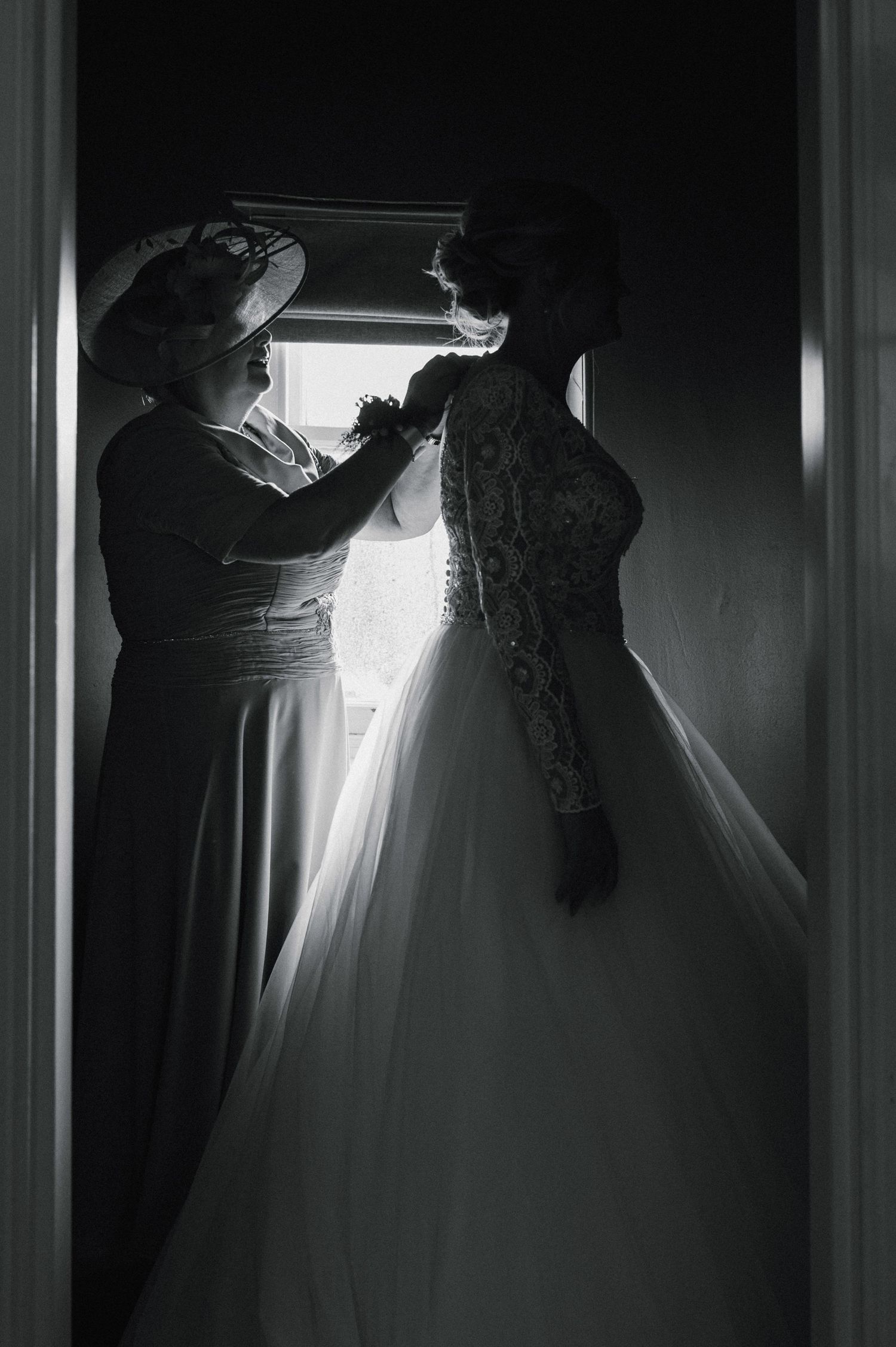 Silhouette of someone adjusting a wedding dress hanging in a doorway.
