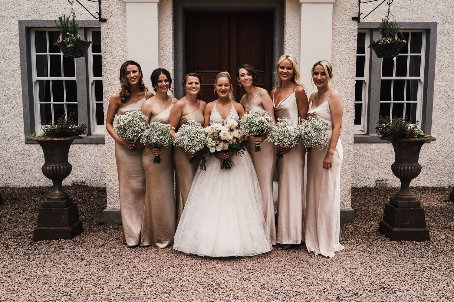 Bridal party in neutral dresses poses together outside a white building with elegant windows.