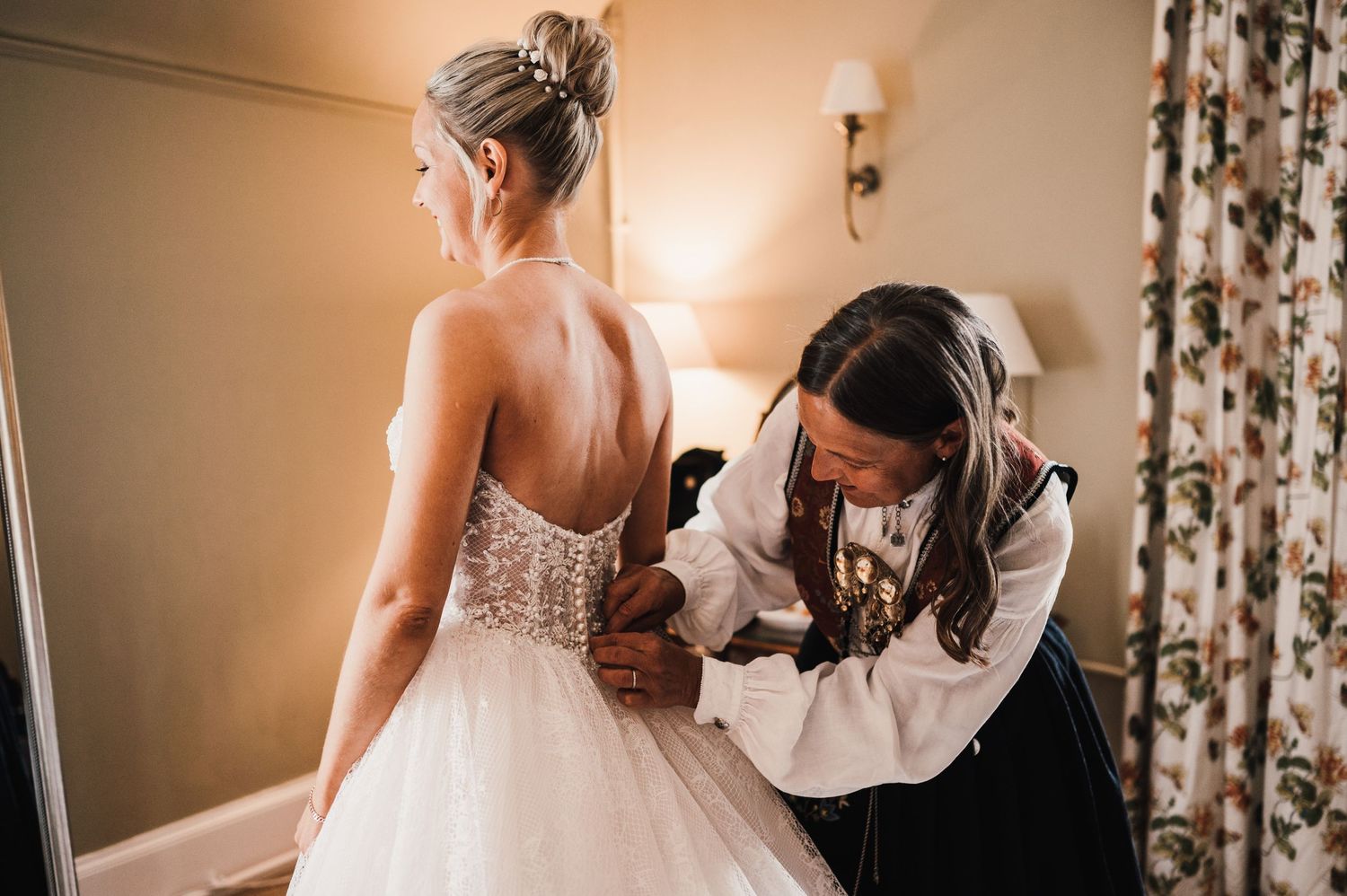 Helper adjusting the back of an elegant white wedding gown with detailed lace bodice.