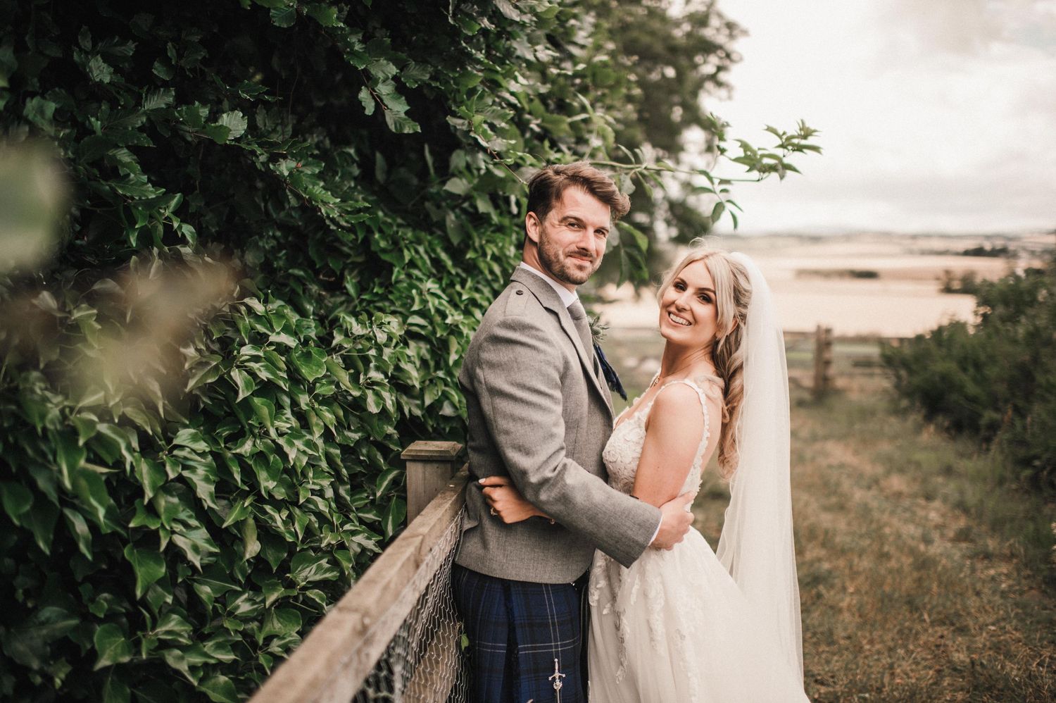 A romantic wedding couple embraces on a balcony overlooking scenic countryside views.