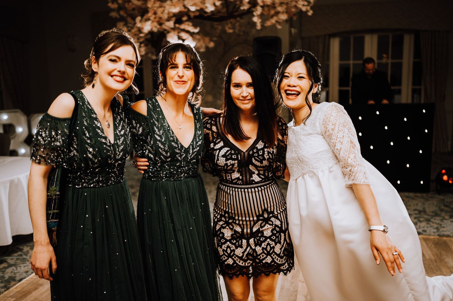 Group shot of friends in elegant dresses at an evening celebration with twinkle lights.
