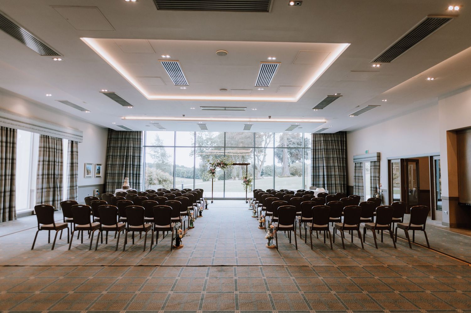 Empty event space with rows of chairs and large windows overlooking garden.