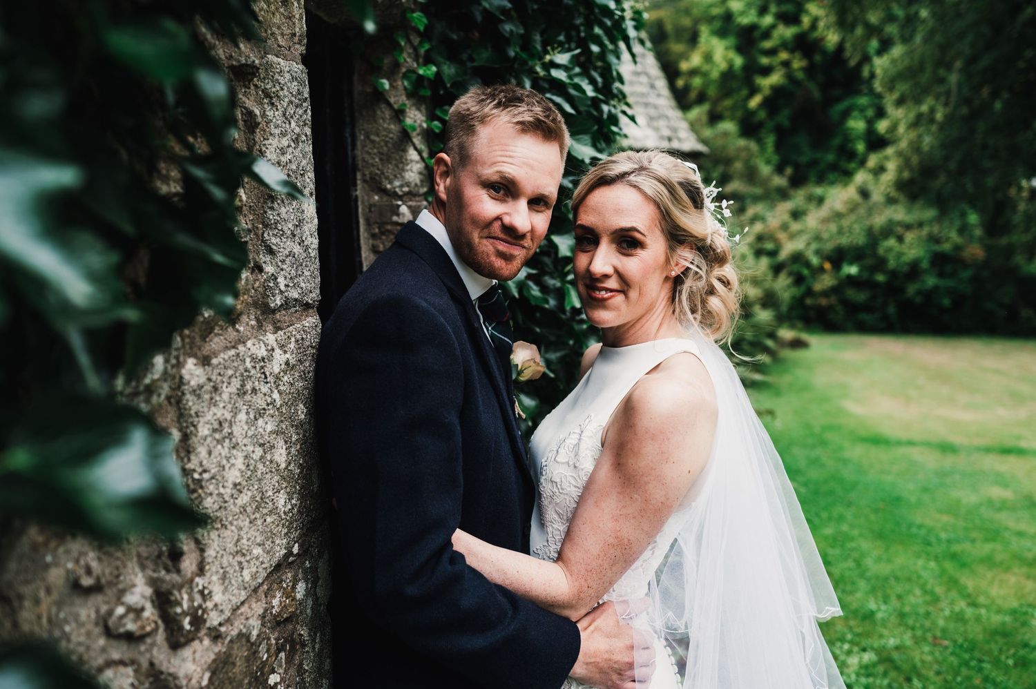 Romantic portrait of couple embracing against stone wall at Scottish estate.