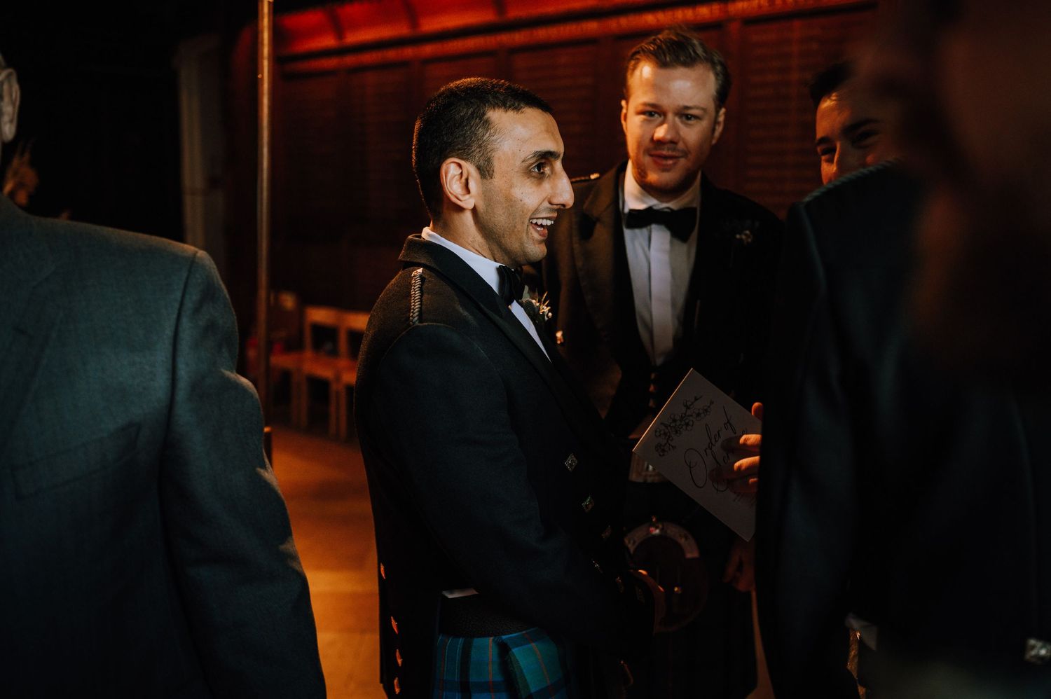 Groomsmen chatting in formal attire during evening wedding reception.