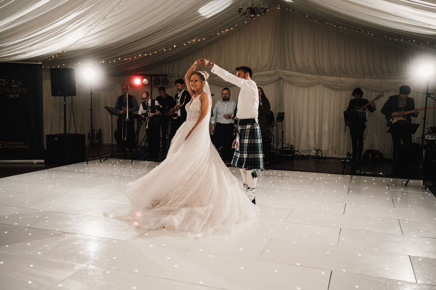 Newlyweds sharing their first dance in a beautifully lit wedding reception tent.