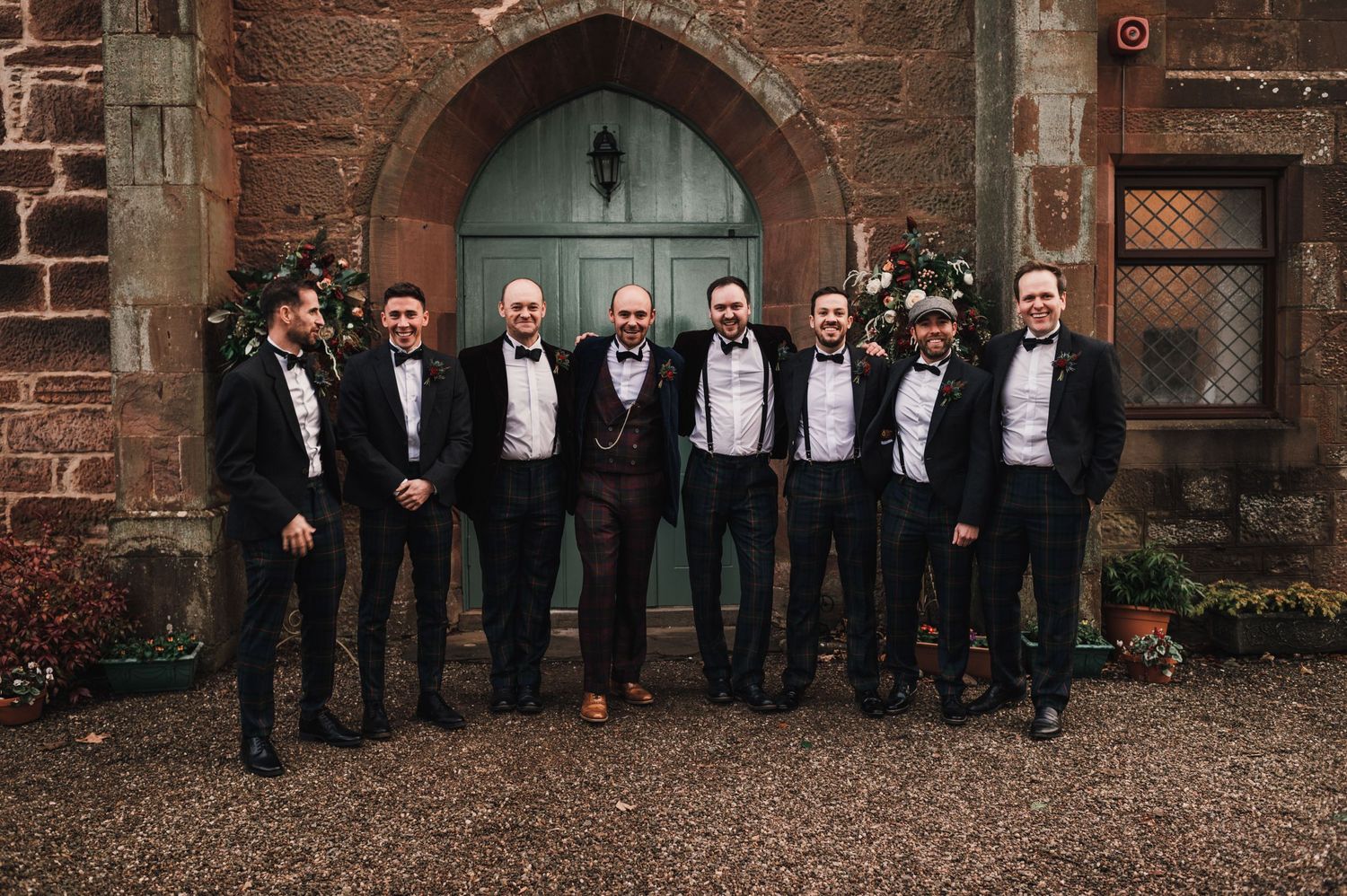 Groomsmen in black suits pose in front of blue church door with stone archway.
