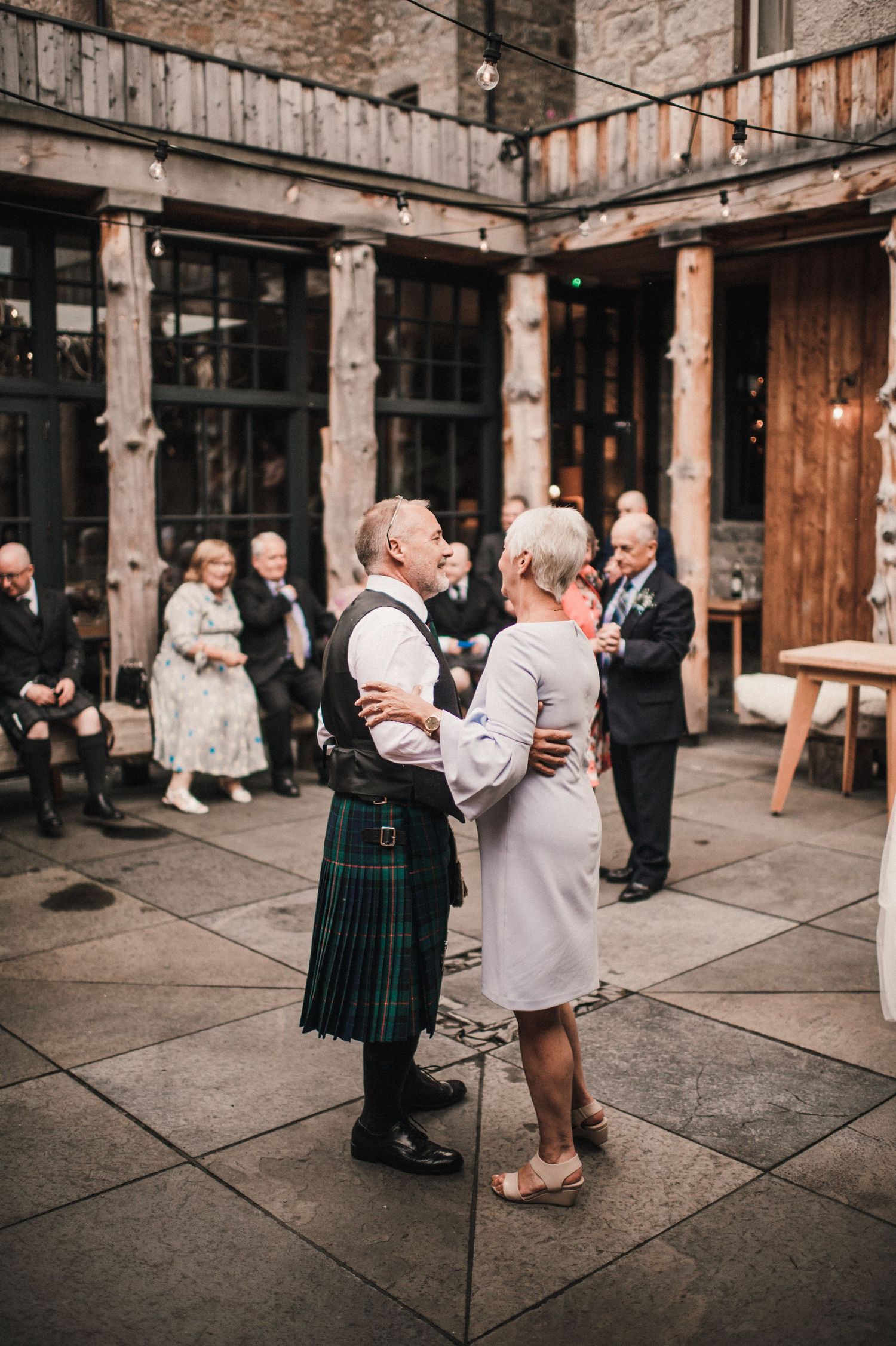 Couple dancing in traditional Scottish dress at historic courtyard reception.