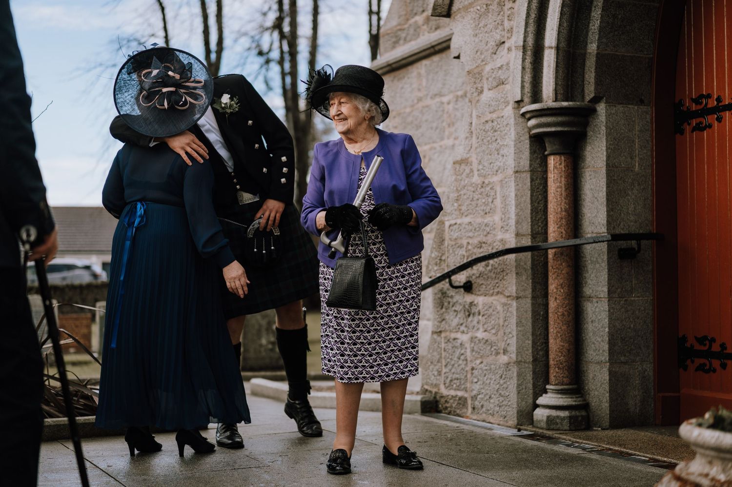 Guests in formal attire gathering outside a stone church entrance.