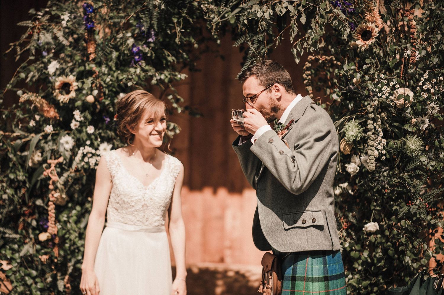 A charming wedding couple sharing a joyous moment surrounded by beautiful foliage and flowers.