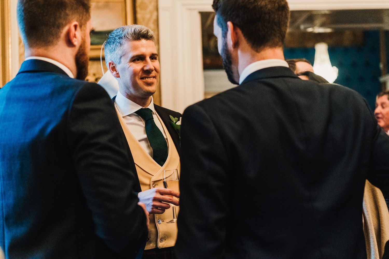 Guests in formal attire share drinks and conversation at an elegant indoor reception.