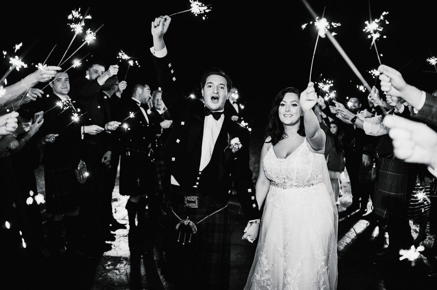Wedding couple celebrates under sparklers held by wedding guests during nighttime reception exit.