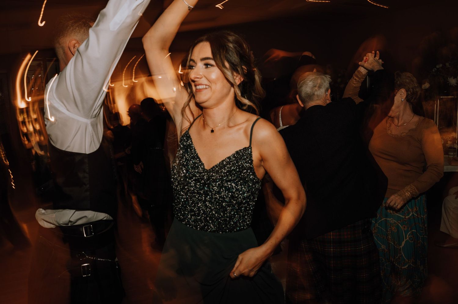 A guest dances enthusiastically in a sparkly black dress at a dimly lit reception.