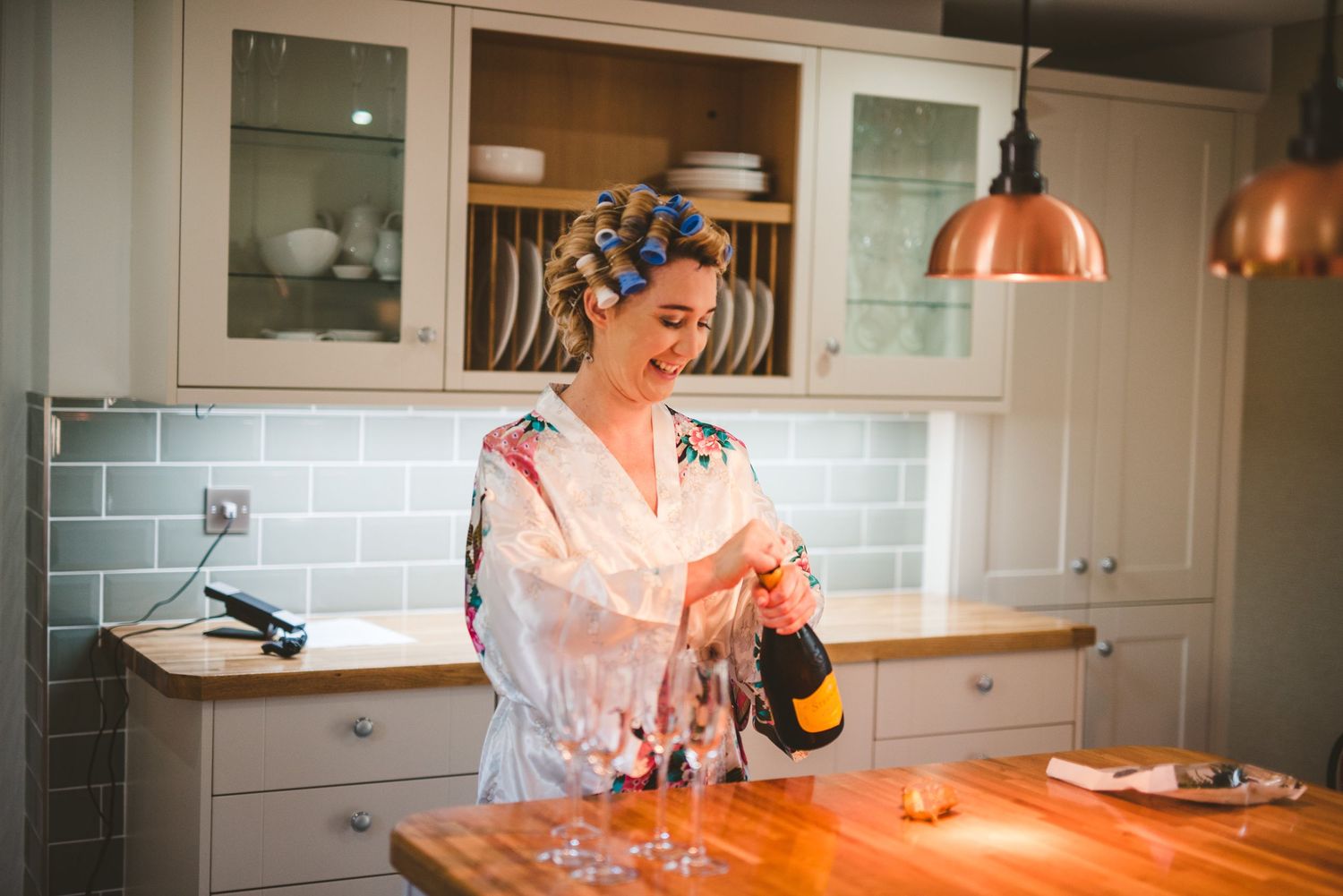 A person in a white coat works in a modern kitchen with copper pendant lights and blue subway tile backsplash.