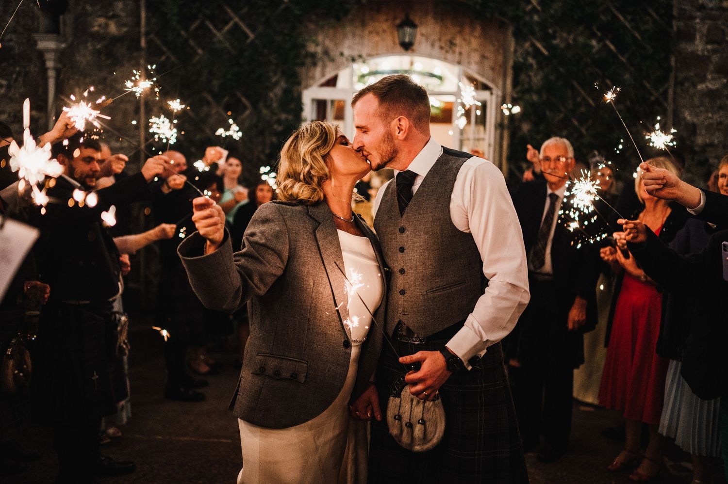 Wedding couple surrounded by guests holding sparklers during evening celebration.