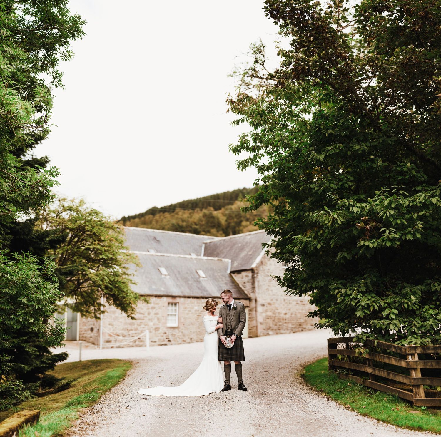 A scenic country road leads to stone buildings and trees on a rural estate.
