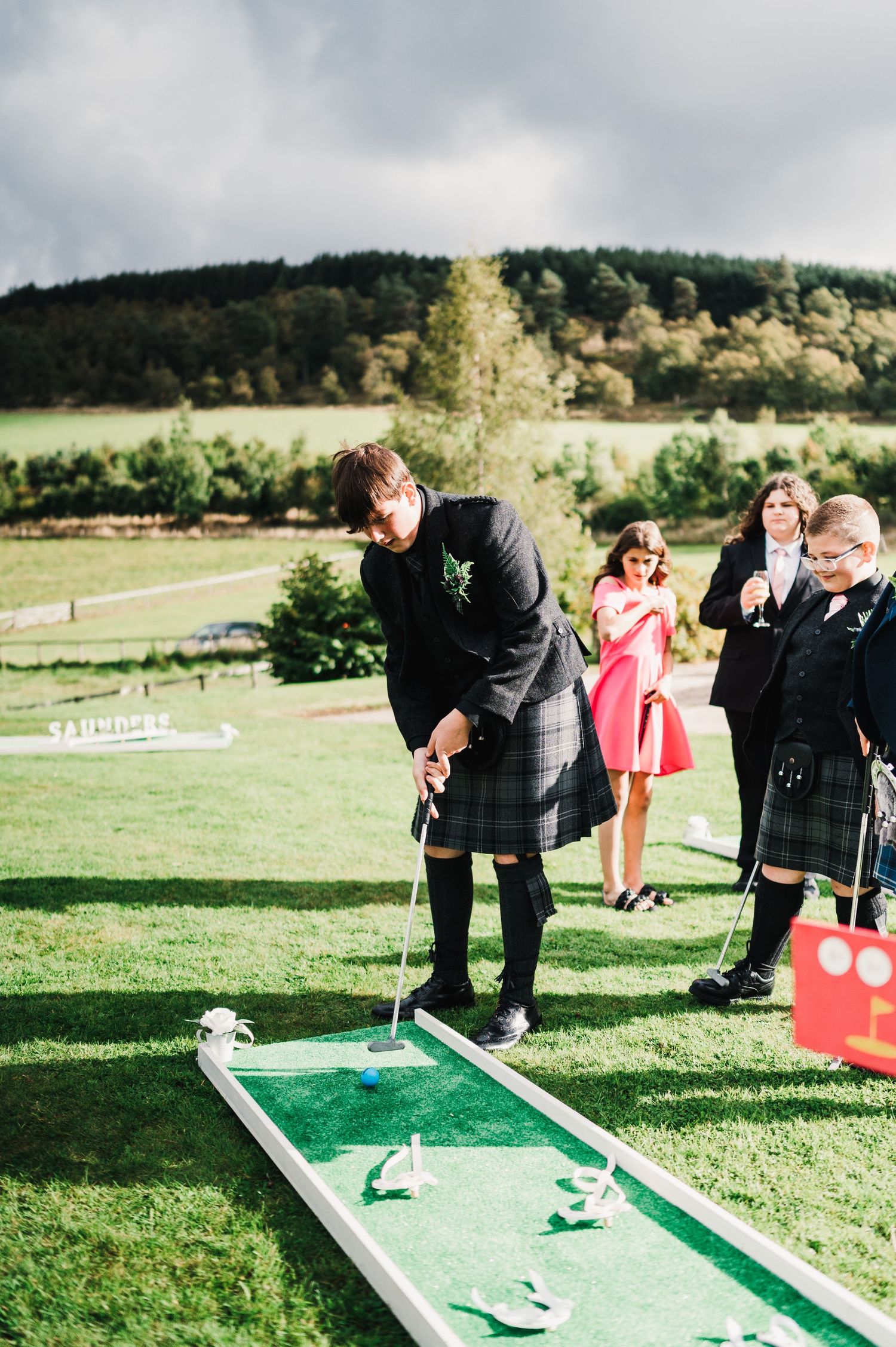 Wedding guests play miniature golf on portable green course set up outdoors.